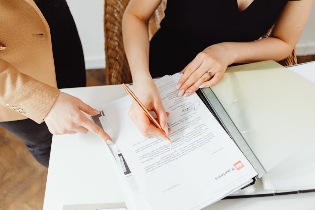 Two women signing important documents at an office desk, showcasing teamwork.